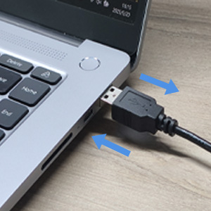 Due cavi USB collegati a una porta per laptop, con connettori blu puntati su una superficie grigia.